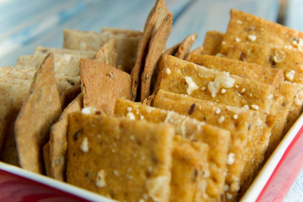 Beberapa potong cracker renyah berwarna cokelat keemasan tersusun rapi dalam wadah merah di atas permukaan meja kayu.