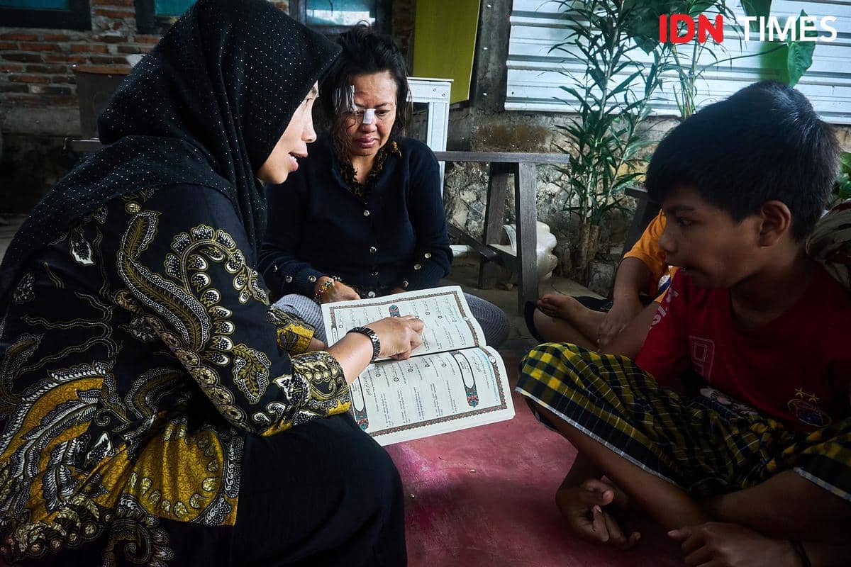 Penyuluh Agama Islam KUA Mijen, Zahrotun Nisa (kiri) mengajarkan bacaan surat pendek Al-Qur'an kepada Ernawati (kedua kiri) dan Marco (kanan), anaknya yang difabel di Semarang, Kamis (15/1/2026). (IDN Times/Dhana Kencana)