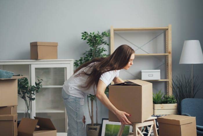 Seseorang membawa kotak kardus di dalam rumah sebagai bagian dari aktivitas memindahkan atau menata barang.