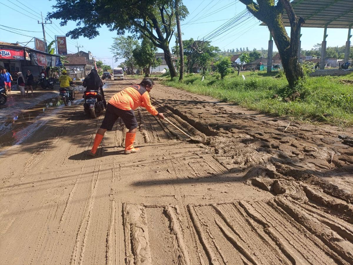 Petugas membersihkan material lumpur yang tutupi akses jalan. IDN Times/Bramanta Pamungkas