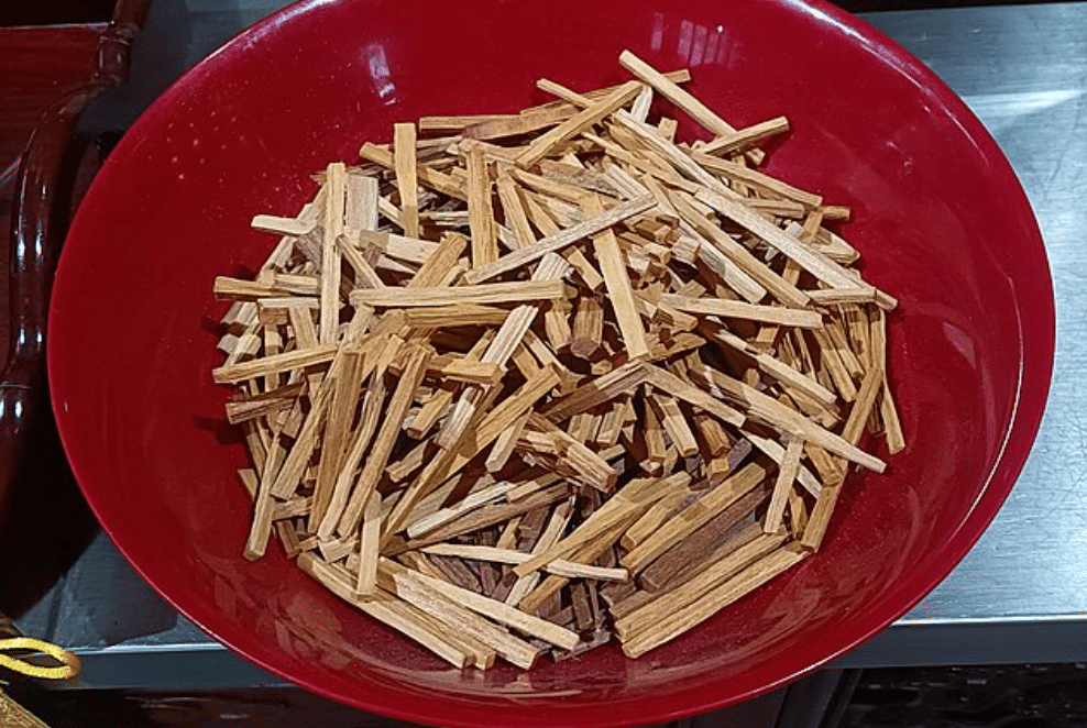 Potongan kecil kayu cendana berwarna cokelat muda hingga tua di dalam mangkuk merah di atas meja logam.