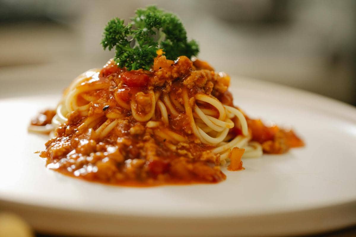 Sepiring spaghetti bolognese dengan saus tomat dan daun basil, disajikan di atas meja sebagai ilustrasi hidangan pasta.