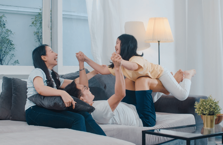 Keluarga tersenyum dan bermain bersama di ruang tamu, menikmati waktu berkualitas di rumah dengan suasana hangat dan bahagia.