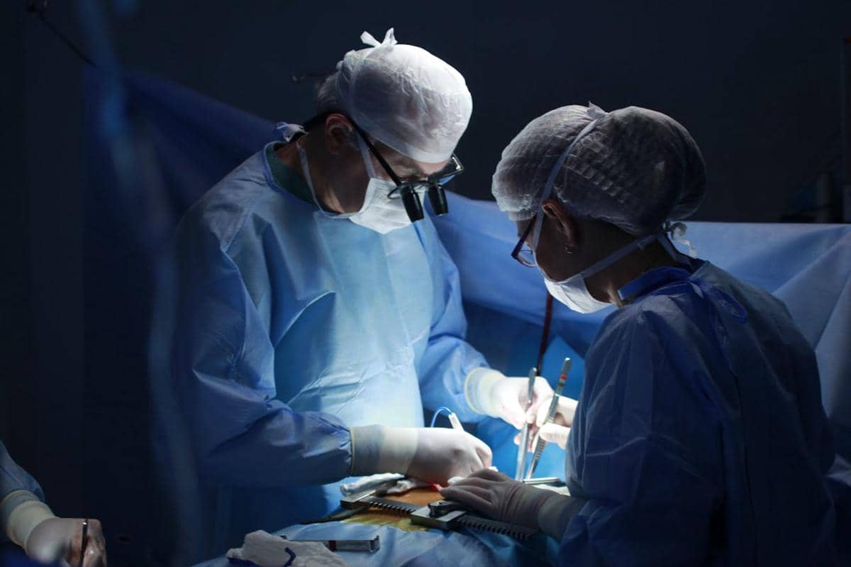 Ilustrasi tenaga medis berseragam bedah melakukan operasi transplantasi ginjal di ruang operasi rumah sakit.
