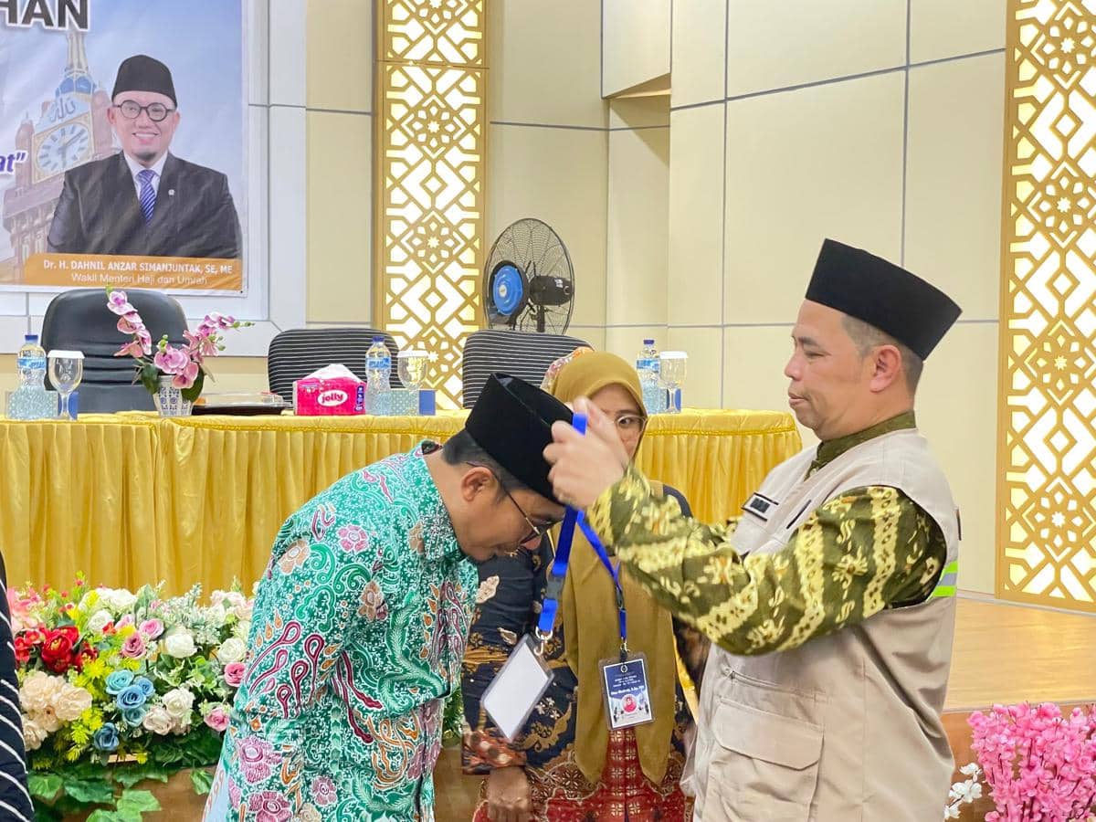 Direktur Jenderal Pengendalian Haji dan Umrah Harun Al Rasyid mengalungkan kokarde kepesertaan kepada salah seorang petugas haji