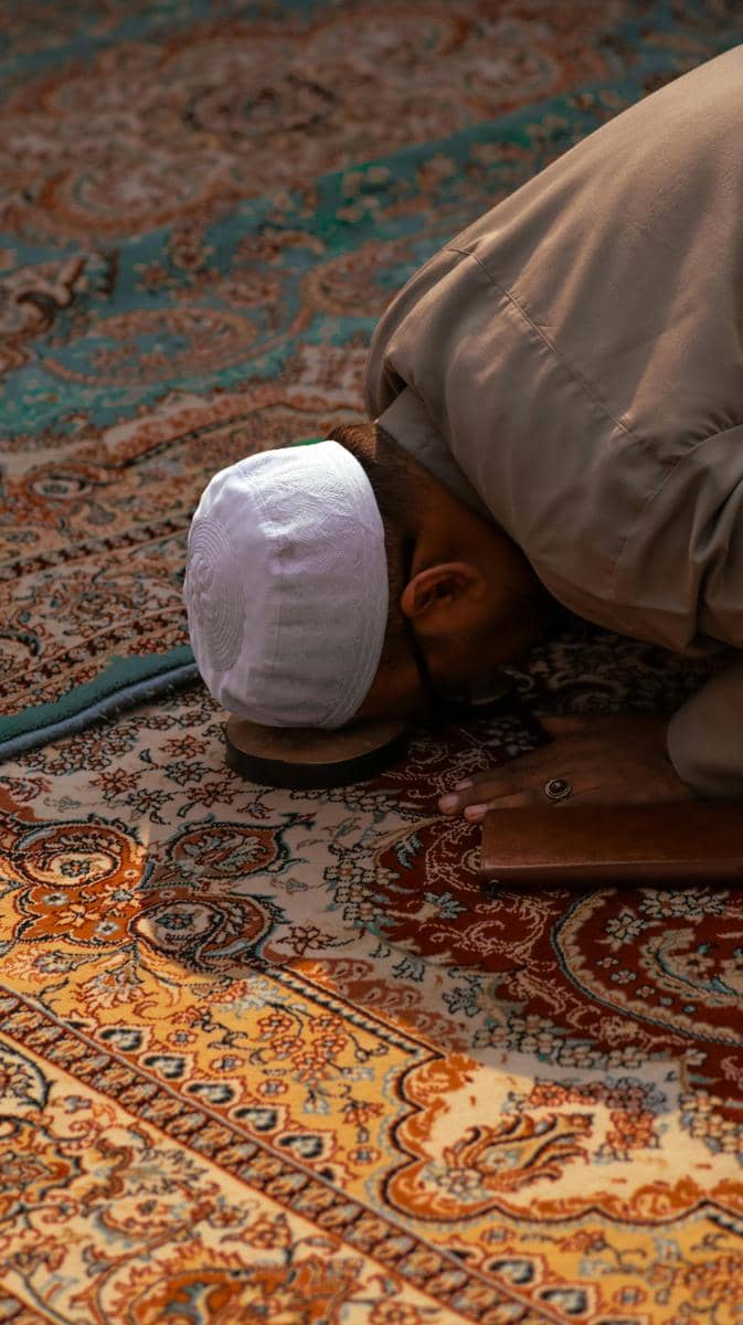 Foto seorang pria bersujud saat salat di atas sajadah dengan peci putih, menggambarkan suasana ibadah dan persiapan spiritual menyambut Ramadan.