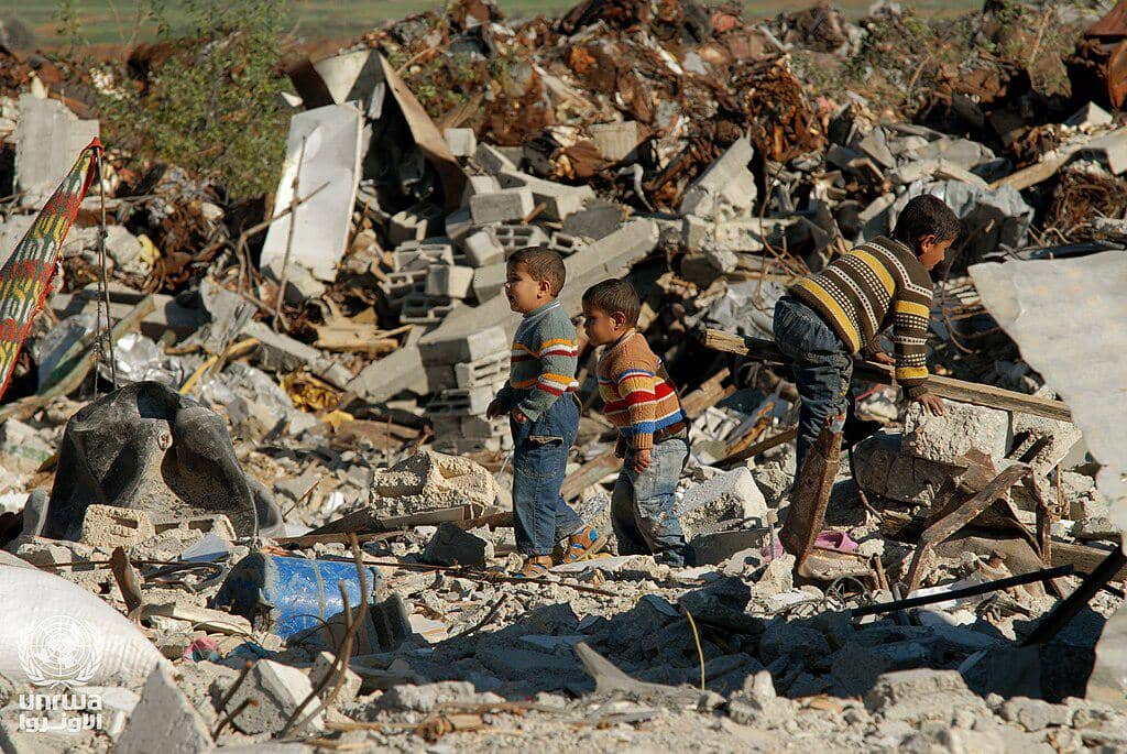 Anak-anak laki-laki menyelamatkan bangunan yang hancur akibat serangan Israel di Jalur Gaza, tahun 2009. (Shareef Sarhan, CC BY-SA 3.0 IGO, via Wikimedia Commons)