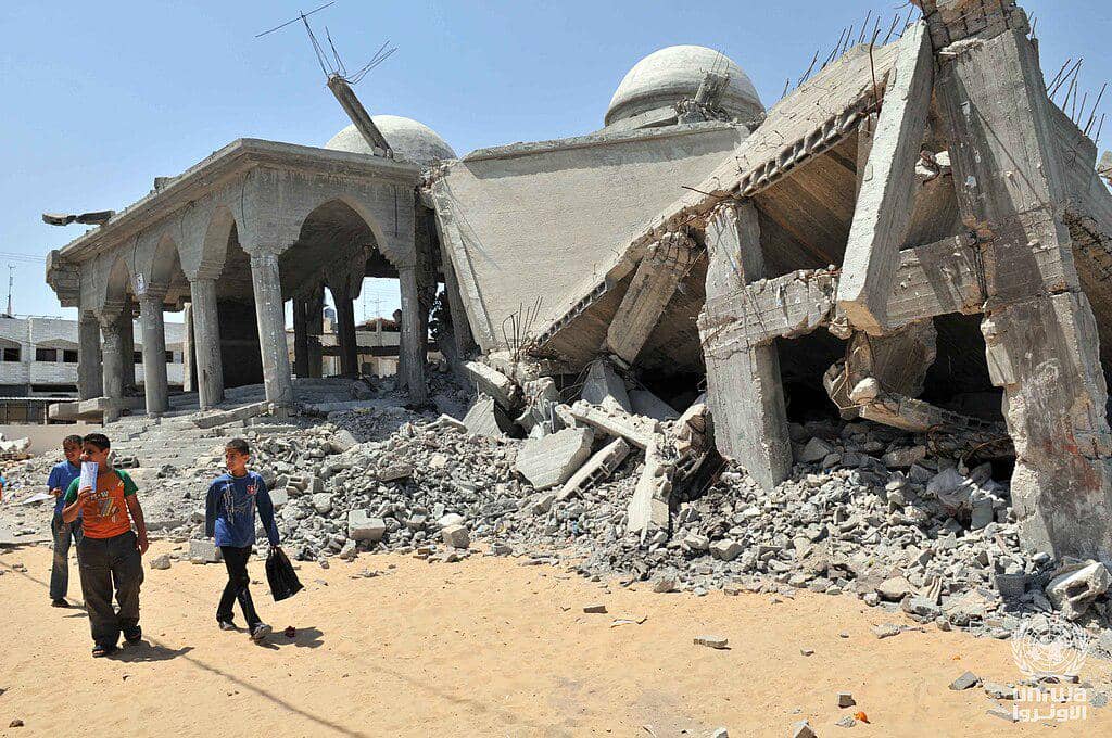 Anak-anak berjalan melewati masjid yang hancur di Jalur Gaza tahun 2009 (Shareef Sarhan, CC BY-SA 3.0 IGO, via Wikimedia Commons)
