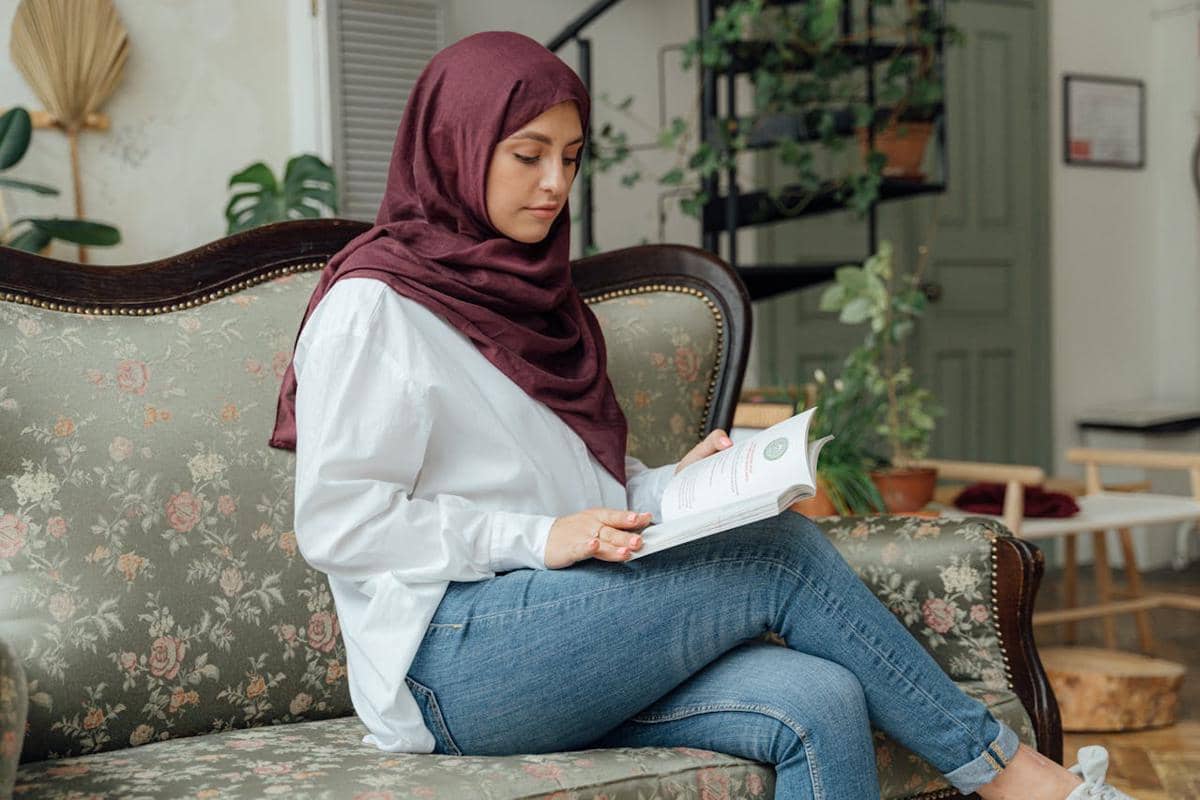 Seorang wanita sedang duduk di kursi sembari membaca buku.