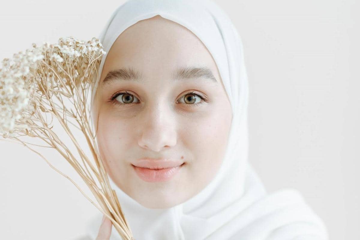 Perempuan muslimah sedang memegang bunga.