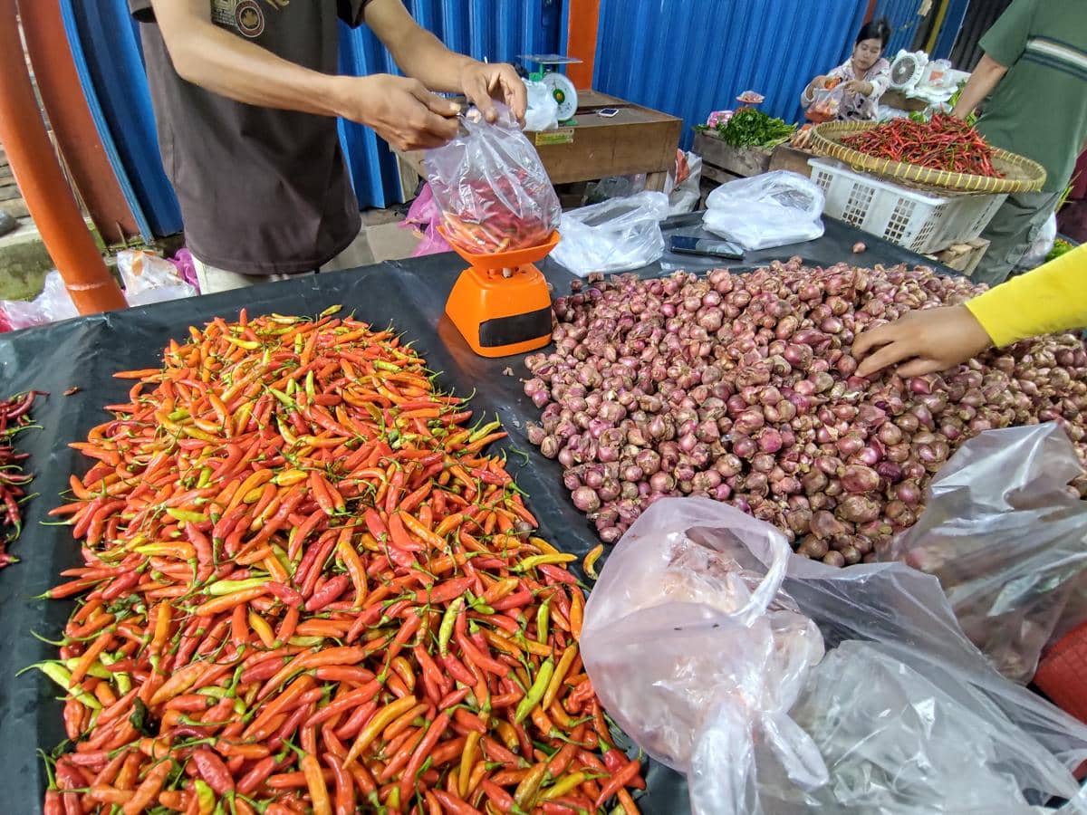 Pedagang cabai dan bawang melayani pembeli di Pasar Randik Sekayu, dengan aneka bahan pangan tersusun di meja dagangan.