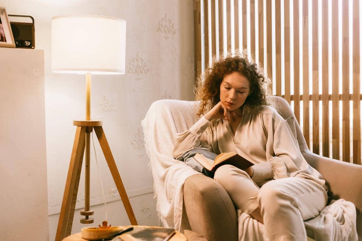 Seorang perempuan sedang membaca buku di sofa.
