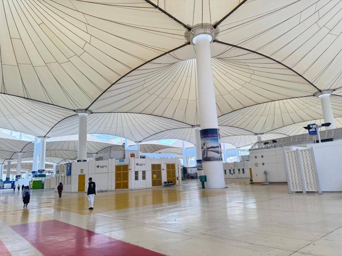 Bagian dalam Terminal Haji Bandara Jeddah di Arab Saudi dengan atap berbentuk kanopi besar dan beberapa orang berjalan di area luas.