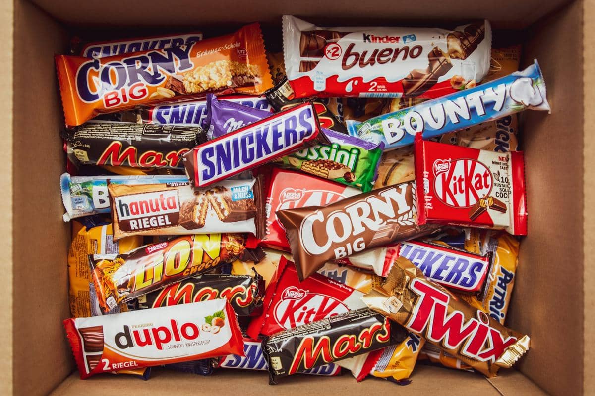 Beragam camilan manis dalam kemasan seperti cokelat batangan dan wafer dengan berbagai merek tersusun di dalam kotak karton.