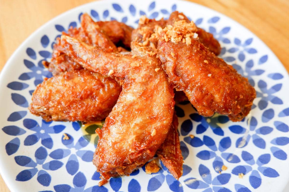 Beberapa potong ayam goreng renyah berwarna keemasan disajikan di atas piring bermotif biru dan putih di atas meja kayu.