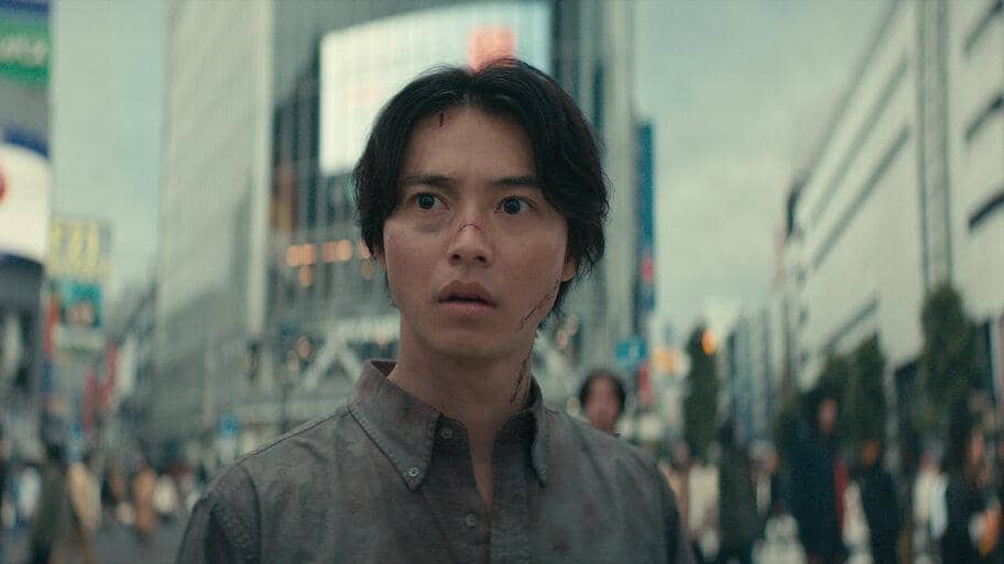 Ryohei Arisu dari Alice in Borderland berdiri dengan latar belakang persimpangan Shibuya yang kosong dan terbengkalai.