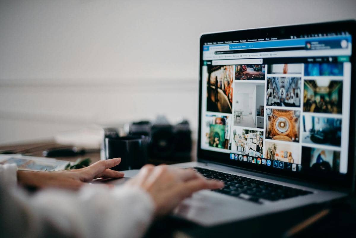 Seseorang menggunakan laptop untuk mengunggah dan melihat berbagai foto di layar, menggambarkan aktivitas penyimpanan cloud.