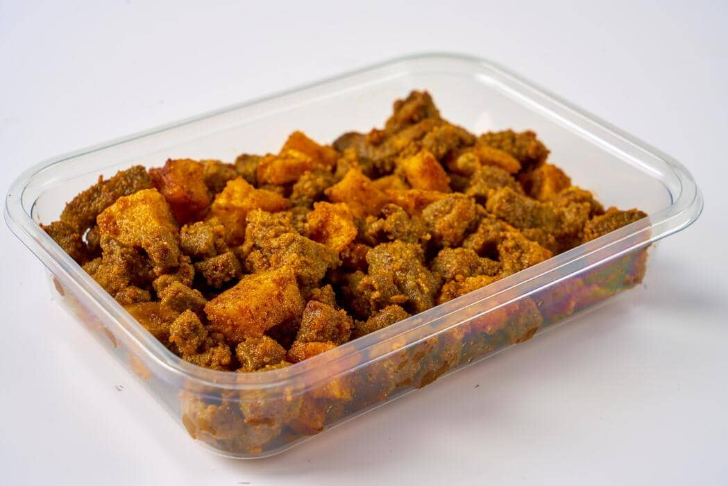 Sambal kentang dengan potongan kentang goreng berwarna keemasan disajikan dalam wadah plastik bening di atas permukaan putih.