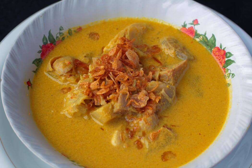 Semangkuk gulai tahu pong berkuah santan kuning dengan lontong, telur rebus, dan taburan bawang goreng.