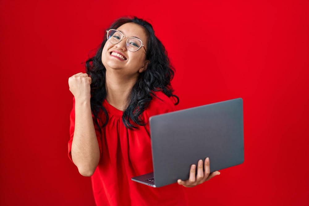 Young asian woman working using computer laptop celebrating victory