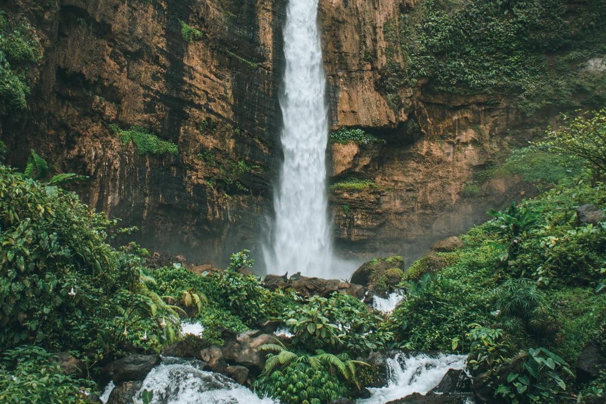 Ilustrasi Air Terjun Kapas Biru dengan nuansa kebiruan yang dikelilingi tebing.