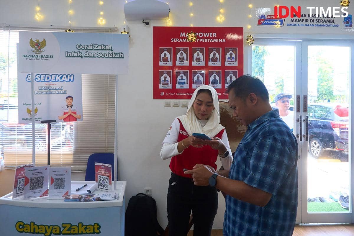 Pemudik Tri Al Trianto (kanan) mengakses aplikasi MyPertamina untuk layanan potong rambut gratis di Serambi MyPertamina di Rest Area KM 379A Tol Semarang–Batang (arah Jakarta ke Semarang), Rabu (18/3/2026). (IDN Times/Dhana Kencana)