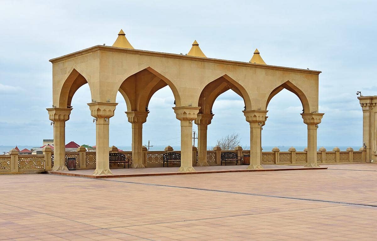 Pelataran Masjid Bibi-Heybat dengan bangunan berarsitektur Islam, kubah, dan menara yang menjulang di bawah langit cerah.