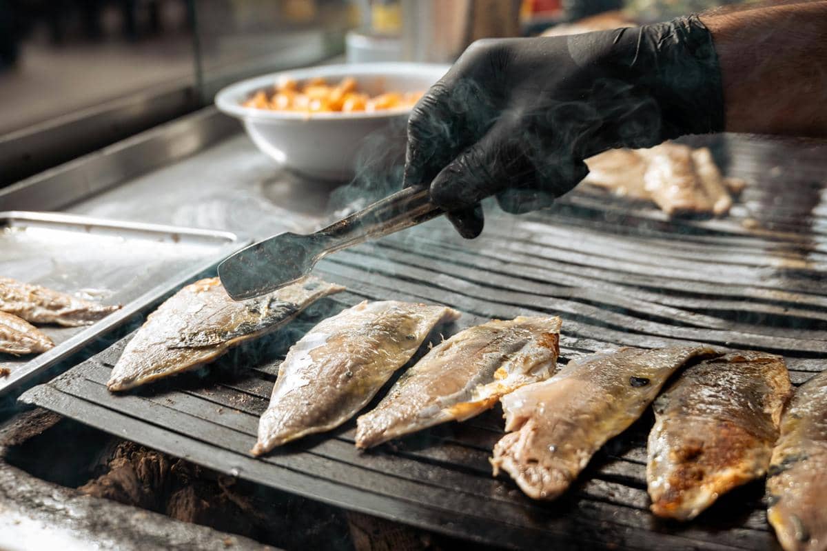 Ilustrasi ikan bakar dan menu seafood dengan suasana warung pantai yang ramai.
