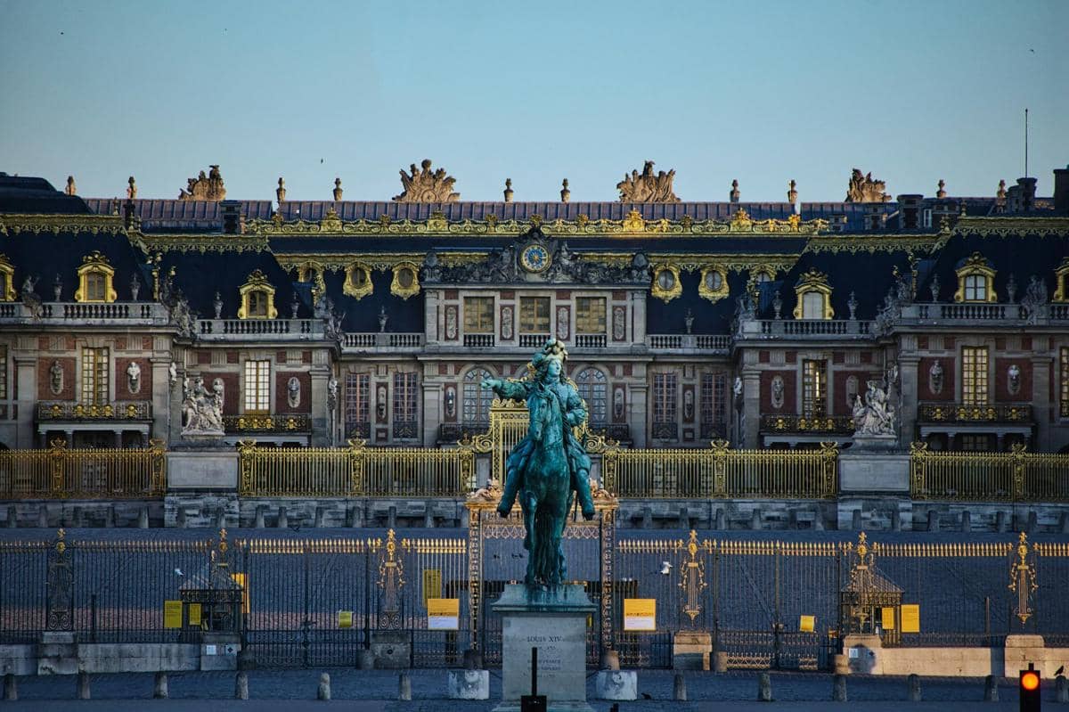 Kemegahan Istana Versailles di Prancis, yang terkenal dengan arsitektur barok dan taman formalnya yang luas, serta patung Raja Louis XIV yang ikonik di depannya.