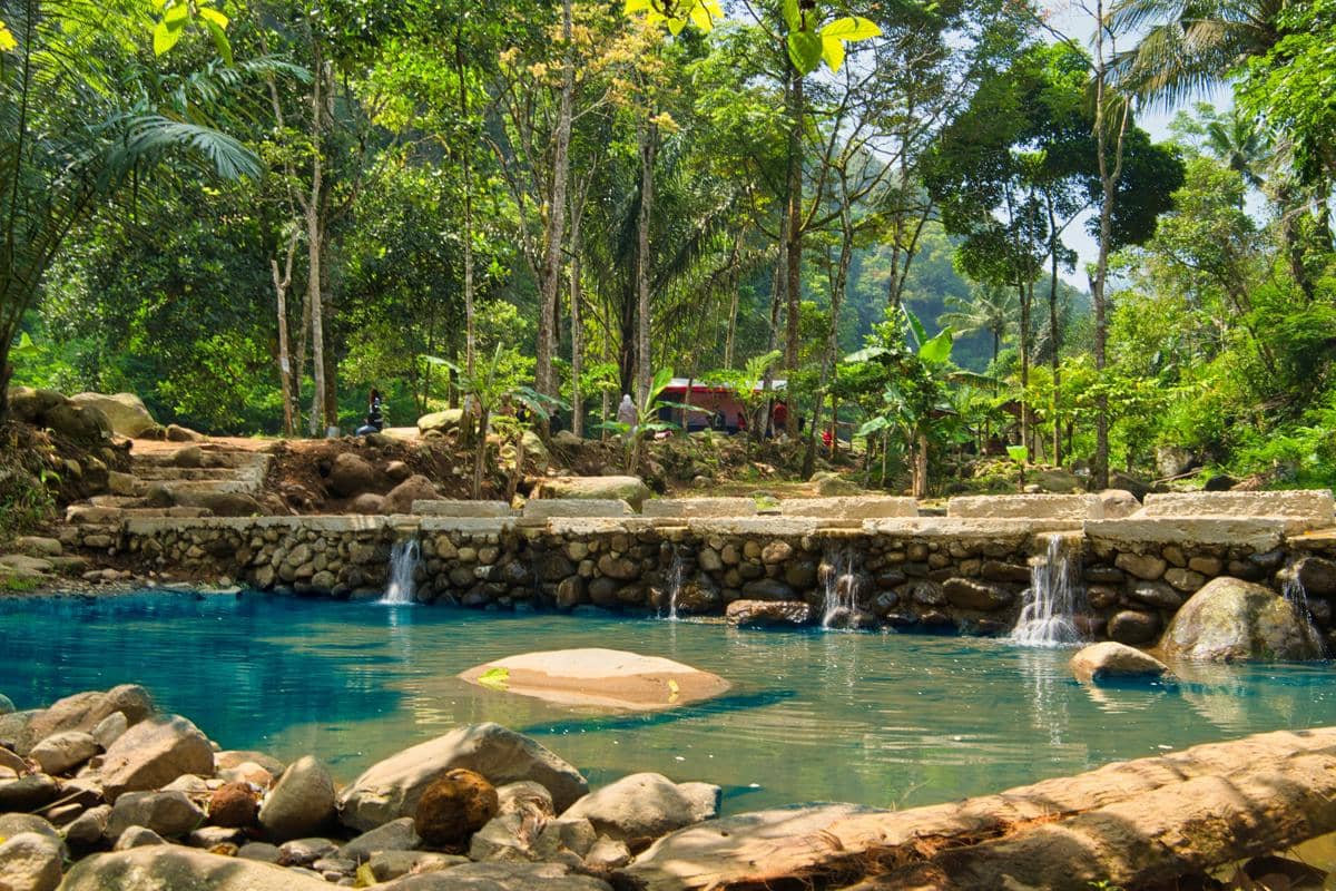 Ilustrasi kolam air panas alami di Pacet dengan latar hutan pinus dan suasana sejuk pegunungan.
