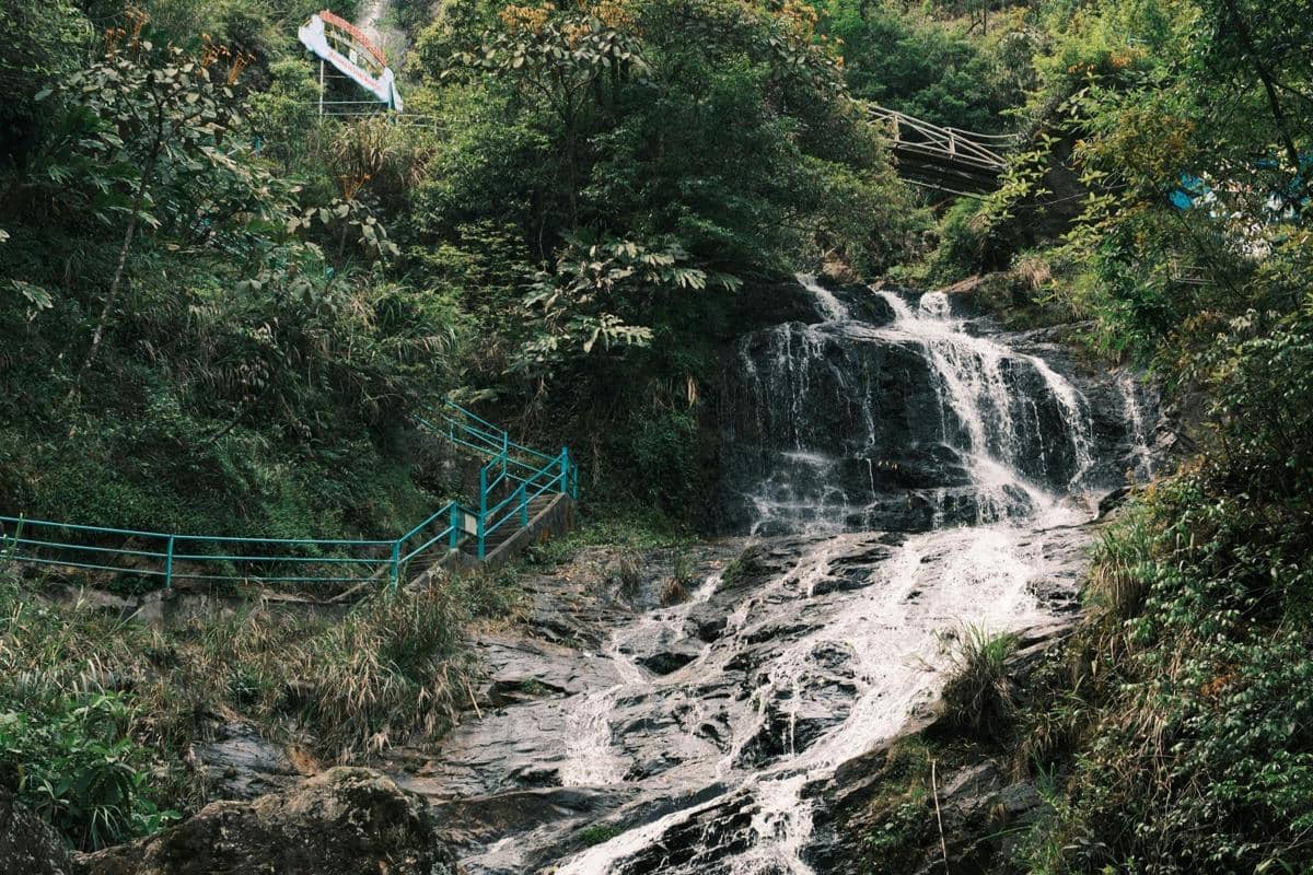 Ilustrasi air terjun tinggi di Pacet dengan latar tebing hijau dan jalur tangga menuju lokasi.