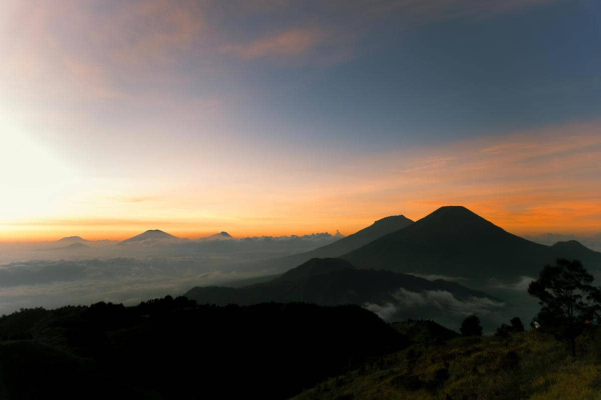 Ilustrasi lautan awan dengan siluet gunung saat matahari terbit.