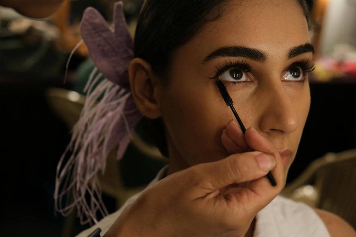 Seorang perempuan mengaplikasikan maskara pada bulu mata dengan kuas kosmetik untuk mempertegas riasan mata.