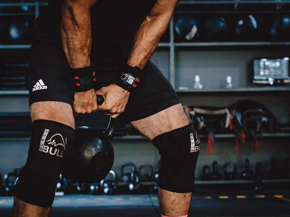 ilustrasi seorang laki-laki mengenakan knee support saat berlatih dengan kettlebell.