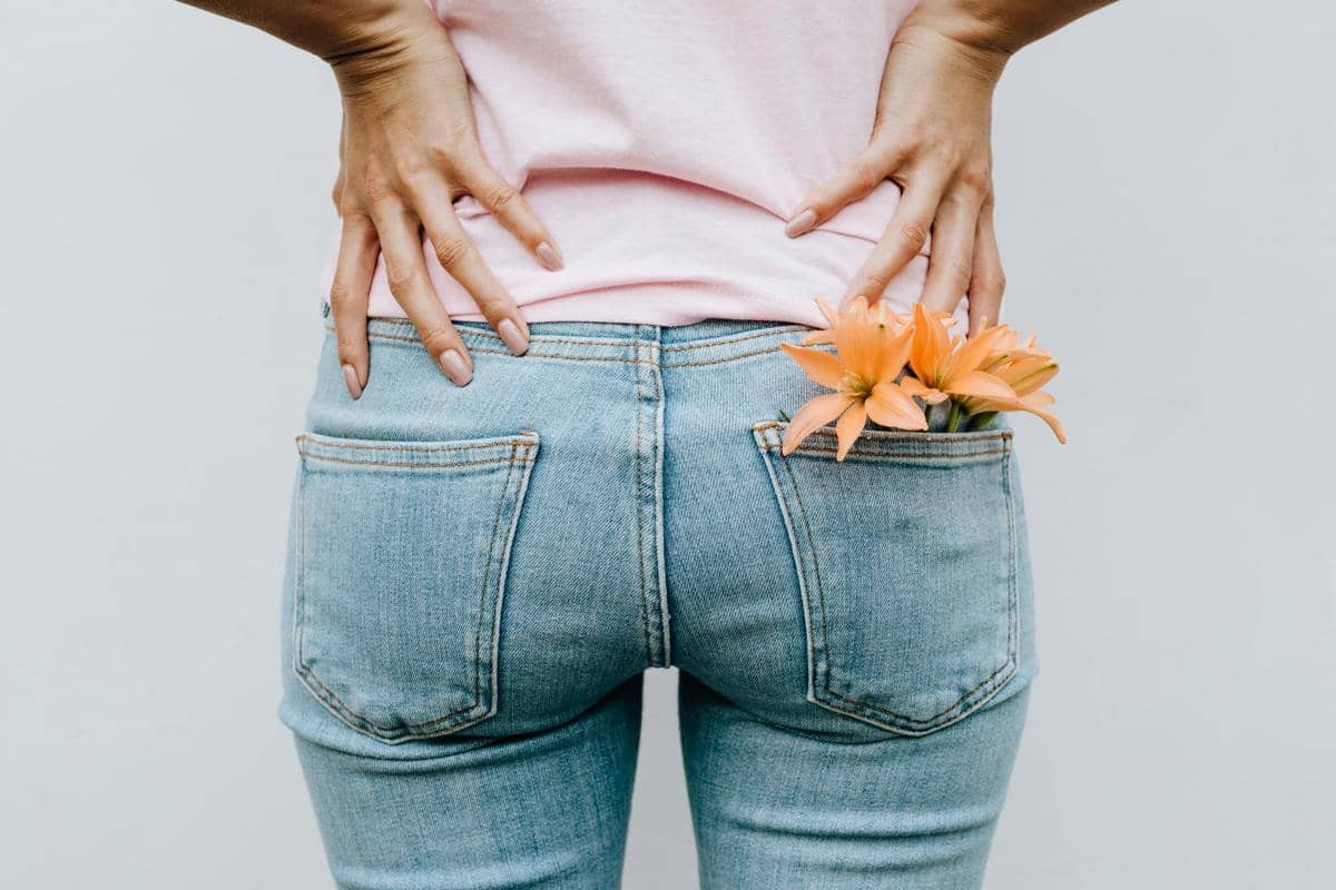 Seseorang mengenakan celana jeans biru dan kaus merah muda dengan tangan di pinggang serta bunga oranye di saku belakang.
