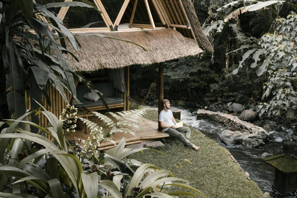 Ilustrasi Toko Kopi Pamanjur dengan gazebo bambu dan aliran sungai alami.