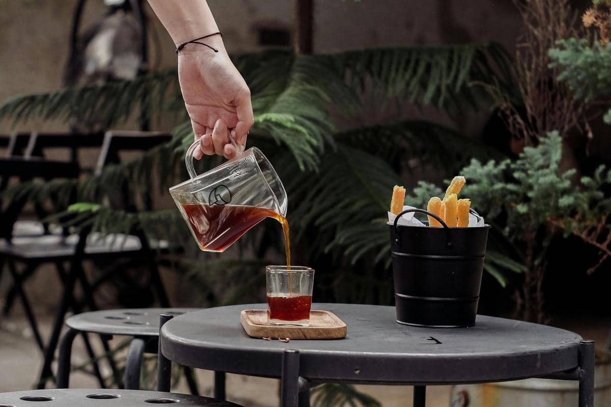 Ilustrasi Warung Mas Doyok Trawas dengan gorengan dan kopi di suasana outdoor.