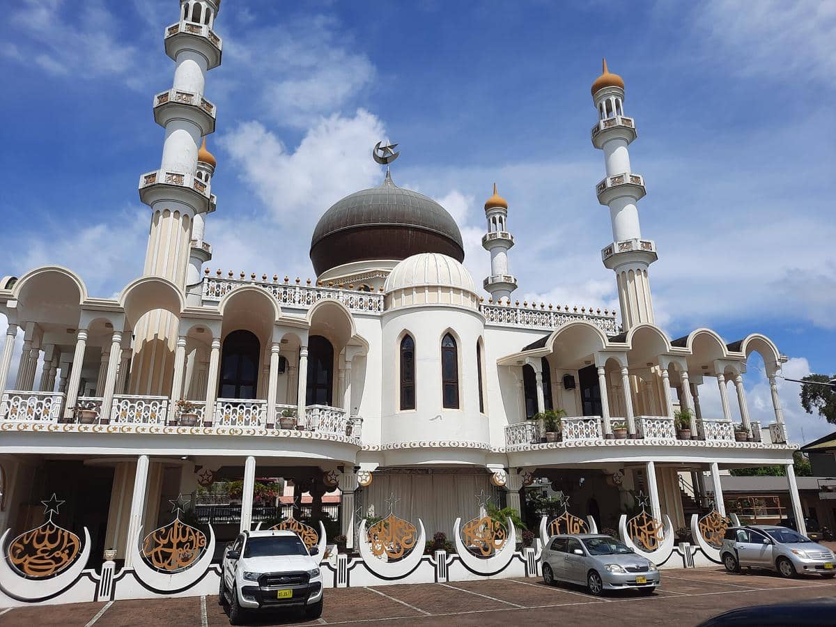 Area parkir di depan Masjid Keizerstraat dengan beberapa mobil terparkir di sepanjang jalan kawasan perkotaan.