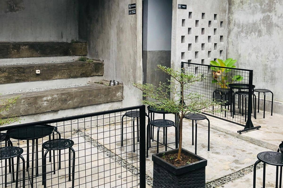 Ilustrasi kafe MASSAL Mojokerto dengan dinding semen terbuka dan konsep industrial.