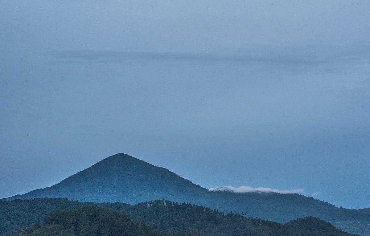 Pemandangan Gunung Putri di Lembang dengan langit biru dan kabut tipis menyelimuti lereng pegunungan di kejauhan.