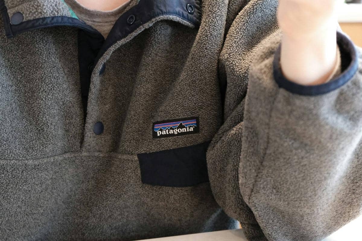 Jaket berbahan fleece berwarna abu-abu dengan detail saku dan kancing di bagian depan, dikenakan oleh seseorang di dalam ruangan.