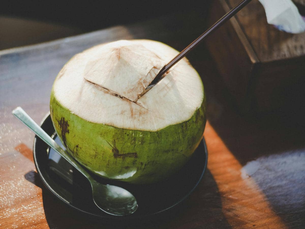 Segelas air kelapa bening dengan potongan kelapa segar sebagai ilustrasi minuman alami yang menyegarkan.