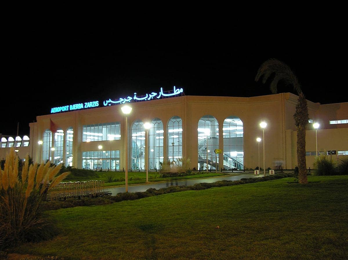 Bangunan Bandara Internasional Djerba-Zarzis di Tunisia tampak terang dengan lampu malam dan taman hijau di depannya.