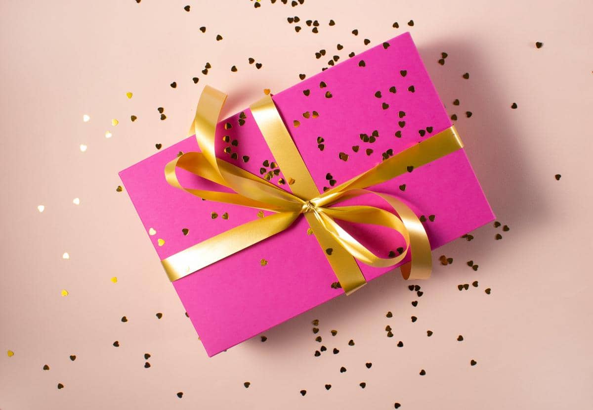 Ilustrasi kado pink dengan pita emas dan confetti