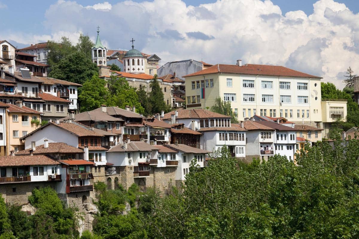 Pemandangan kota Veliko Tarnovo dengan deretan rumah tradisional beratap merah di lereng bukit dan pepohonan hijau di sekitarnya.