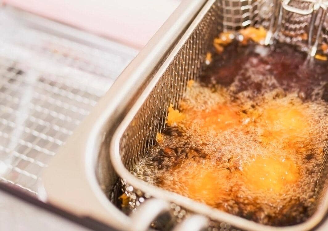 Proses menggoreng makanan dengan teknik deep frying menggunakan minyak panas dalam wadah logam dengan keranjang goreng.