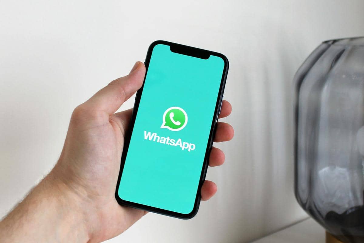 Ilustrasi tangan seseorang memegang ponsel pintar dengan logo WhatsApp di layar.