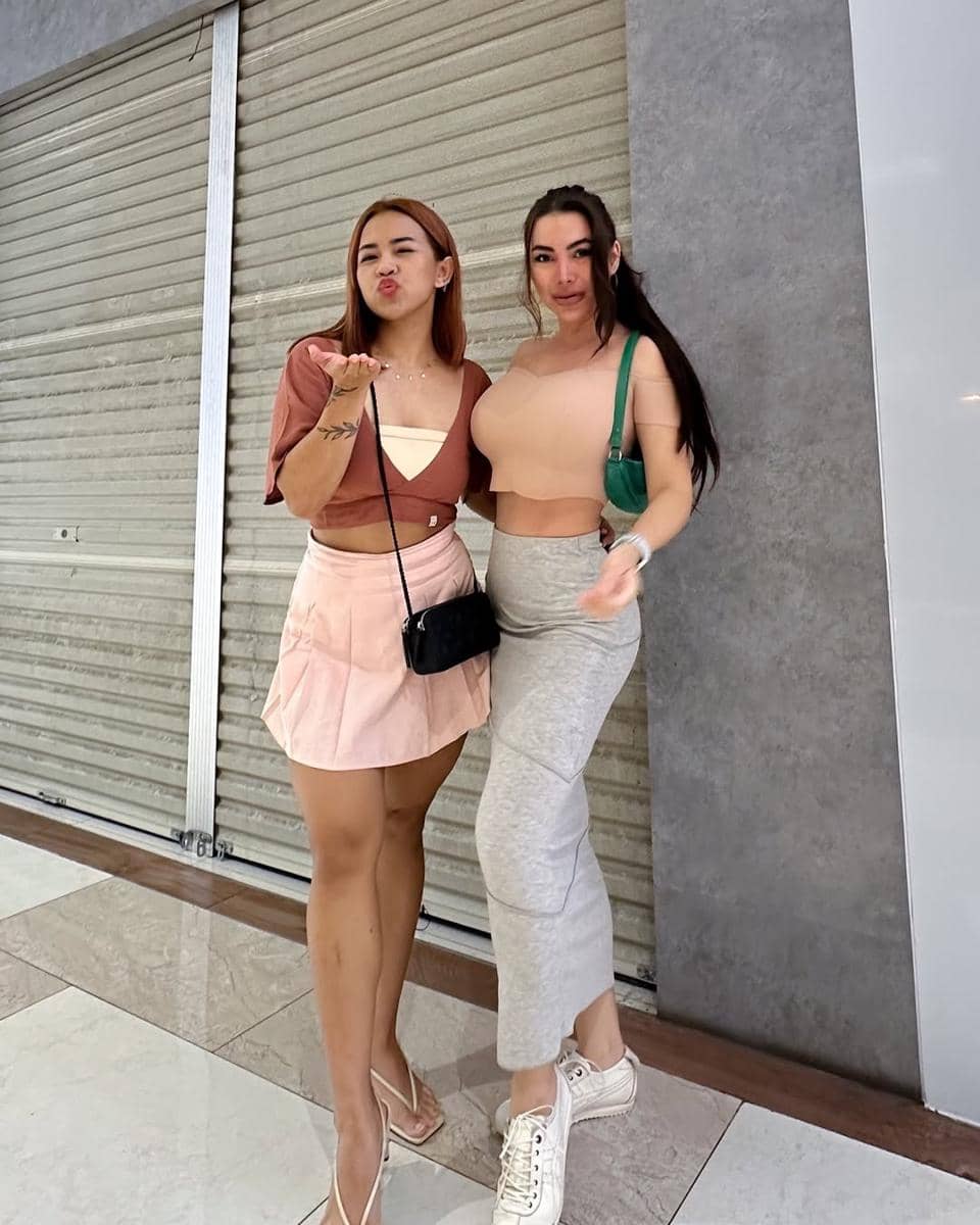 Dua wanita berpose di depan pintu toko tertutup, mengenakan crop top dengan gaya kasual dan tas kecil sebagai aksesori.