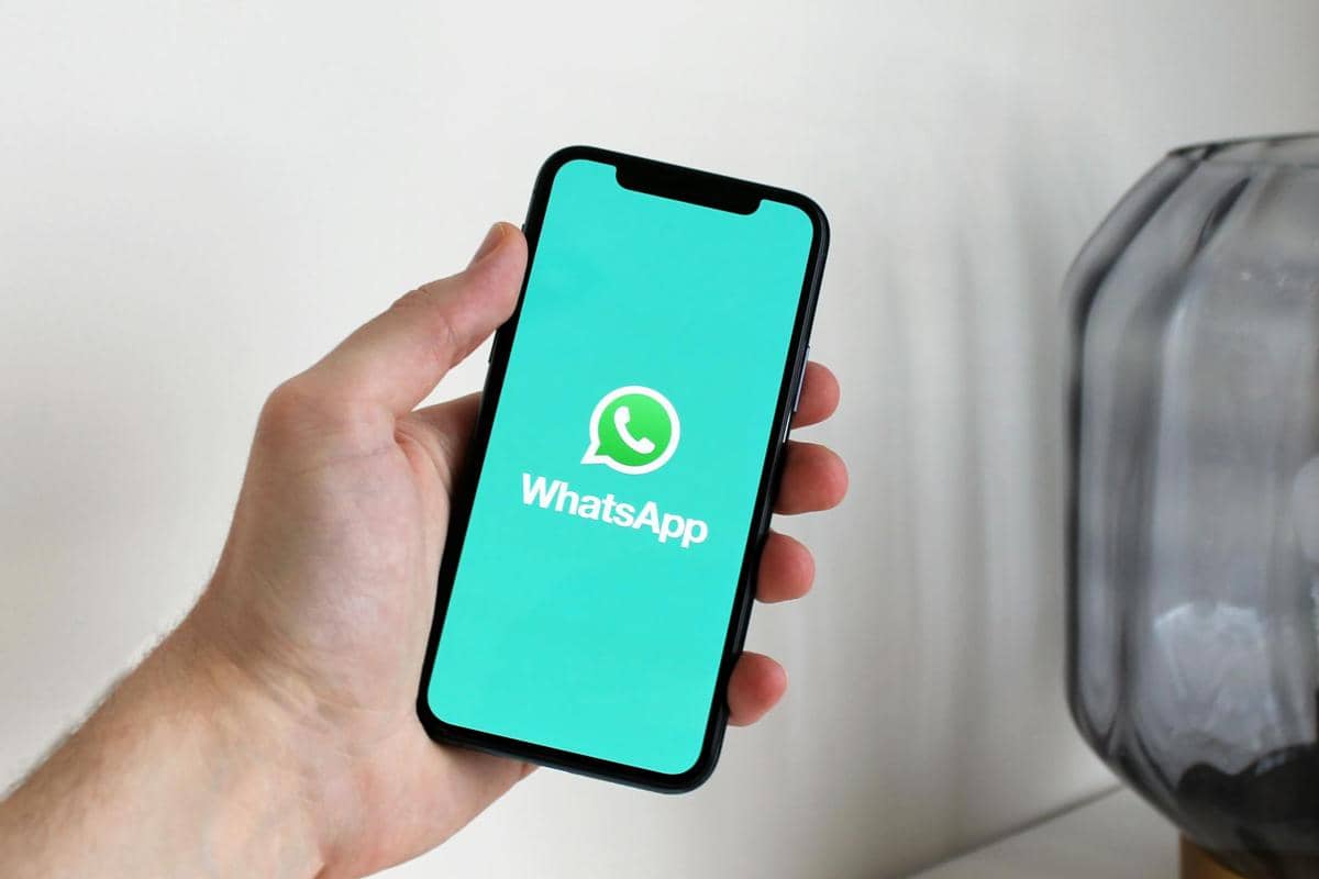 Ilustrasi tangan seseorang sedang memegang ponsel pintar dengan logo WhatsApp di layar
