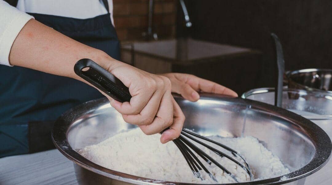 Ilustrasi perempuan mengaduk masakan dalam panci menggunakan sendok kayu di dapur sambil tersenyum.